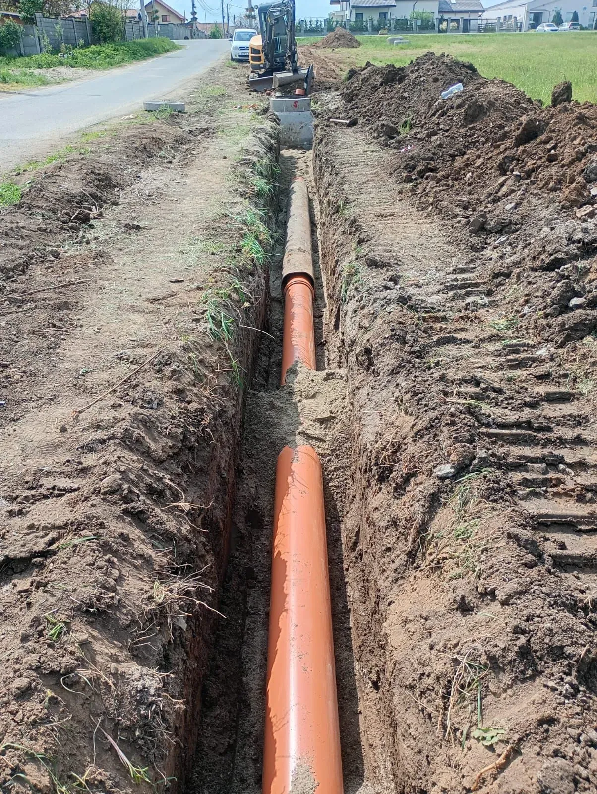 Conductă PVC pozată pe toată lungimea tranșeei, cu excavatorul în capăt