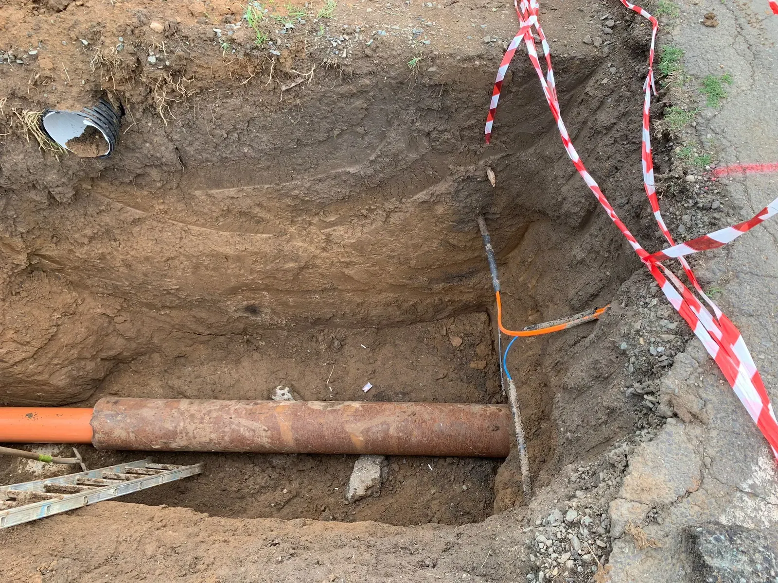 Conductă metalică traversând fundul unei excavații, cu bandă de semnalizare deasupra