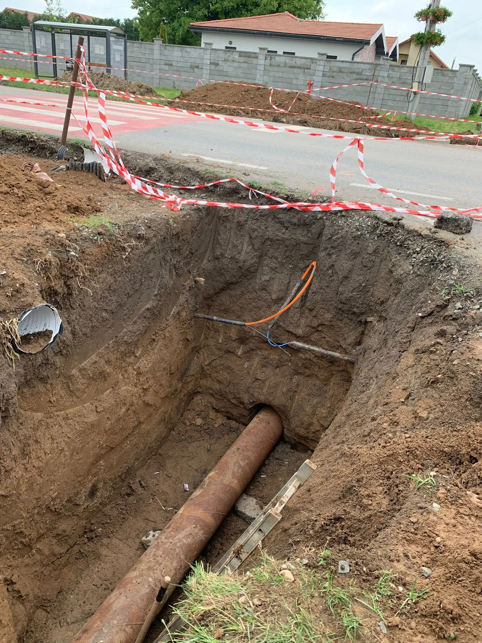 Excavație lângă carosabil, cu semnalizare montată și conductă expusă la bază