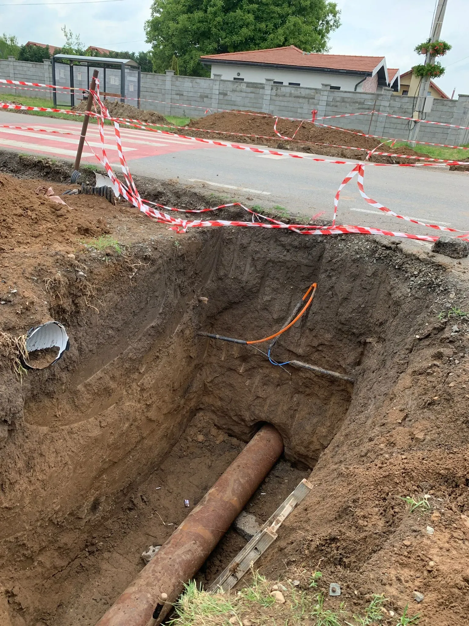 Excavație la marginea drumului, cu conducta existentă expusă și semnalizarea pusă